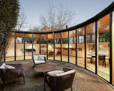 Curved glass-walled living area opening onto a stone terrace