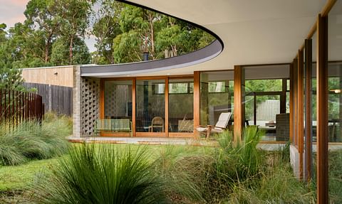 Contemporary architect-designed home with expansive glazing, timber-framed interiors, landscaped gardens and a distinctive curved roof connecting indoor and outdoor spaces.