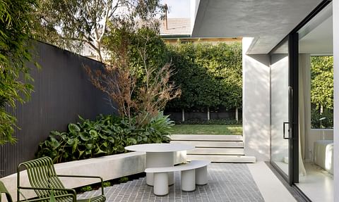 Contemporary outdoor entertaining area with landscaped gardens, stone paving, built-in seating and large sliding doors that extend the home's living spaces outdoors.